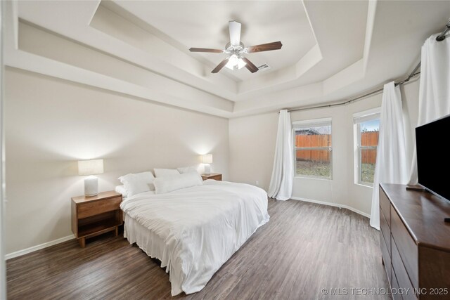 bedroom featuring visible vents, ceiling fan, baseboards, wood finished floors, and a raised ceiling