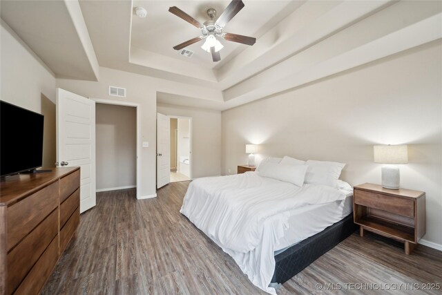 bedroom with a tray ceiling, baseboards, dark wood-type flooring, and visible vents