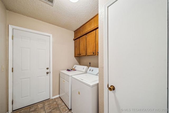 clothes washing area with stone finish floor, cabinet space, independent washer and dryer, and a textured ceiling