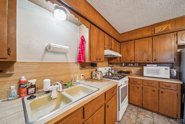 kitchen with white appliances, brown cabinetry, a sink, light countertops, and under cabinet range hood