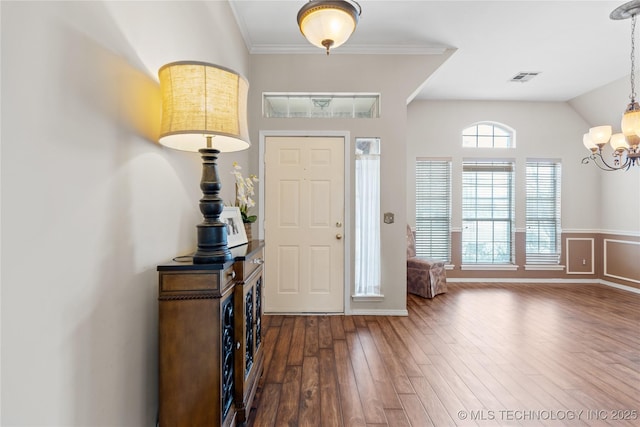 entrance foyer with visible vents, a notable chandelier, dark wood finished floors, and ornamental molding