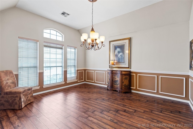 unfurnished dining area featuring visible vents, a chandelier, vaulted ceiling, wainscoting, and dark wood-style floors