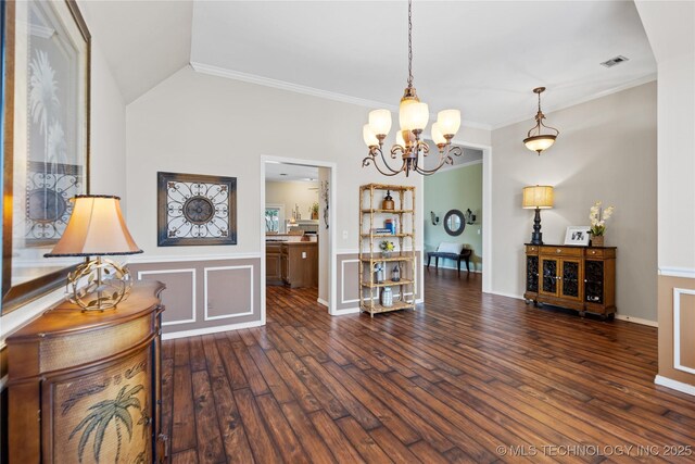 interior space featuring visible vents, ornamental molding, hardwood / wood-style flooring, wainscoting, and lofted ceiling