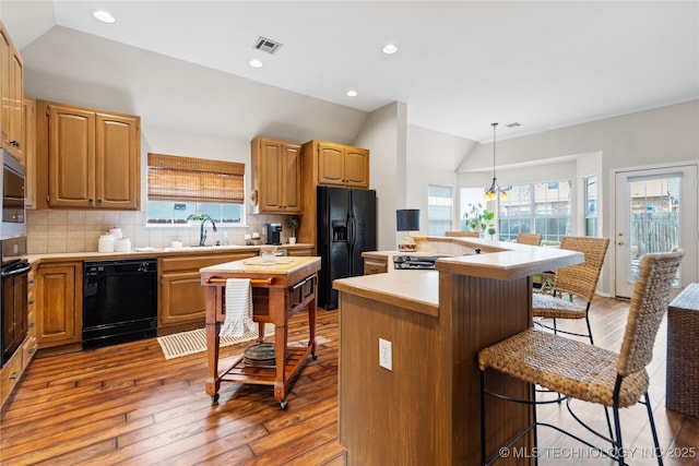 kitchen with visible vents, black appliances, a breakfast bar, decorative backsplash, and lofted ceiling