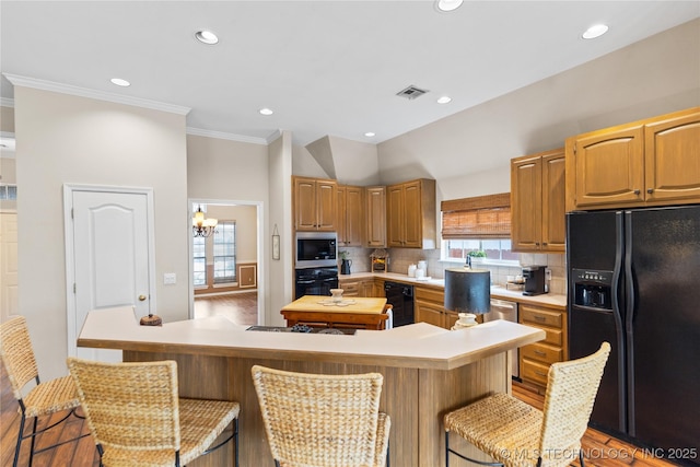 kitchen with visible vents, black appliances, a breakfast bar, light countertops, and decorative backsplash