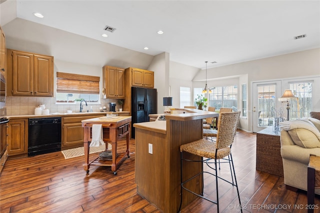 kitchen with visible vents, lofted ceiling, black appliances, a kitchen bar, and tasteful backsplash