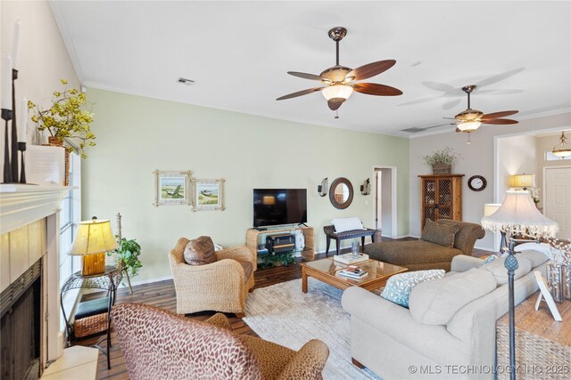 living area featuring visible vents, wood finished floors, a tiled fireplace, and crown molding