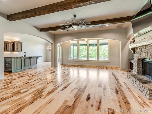 12491 S 105th Ave E, Bixby, OK 74008 - unfurnished living room featuring arched walkways, light wood-style floors, a fireplace, a ceiling fan, and baseboards