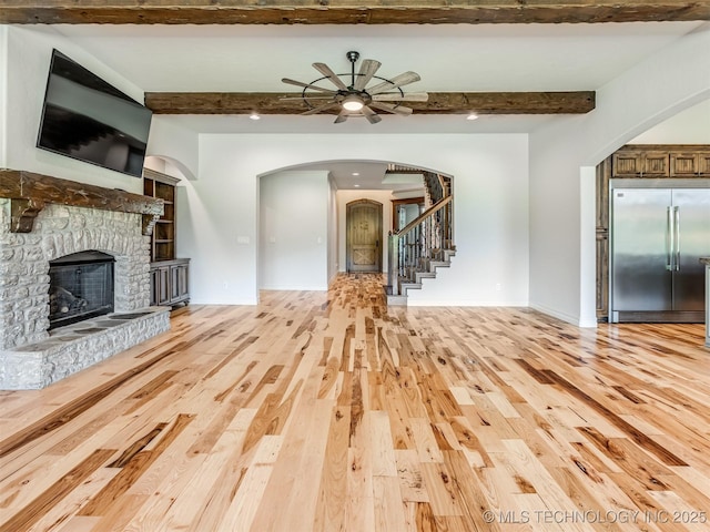 12491 S 105th Ave E, Bixby, OK 74008 - unfurnished living room featuring beamed ceiling, arched walkways, light wood-style flooring, a stone fireplace, and stairway