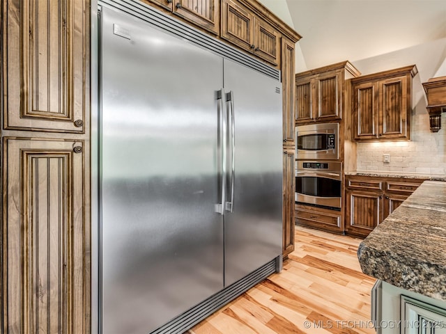 12491 S 105th Ave E, Bixby, OK 74008 - kitchen featuring built in appliances, light wood-style floors, backsplash, and dark stone countertops