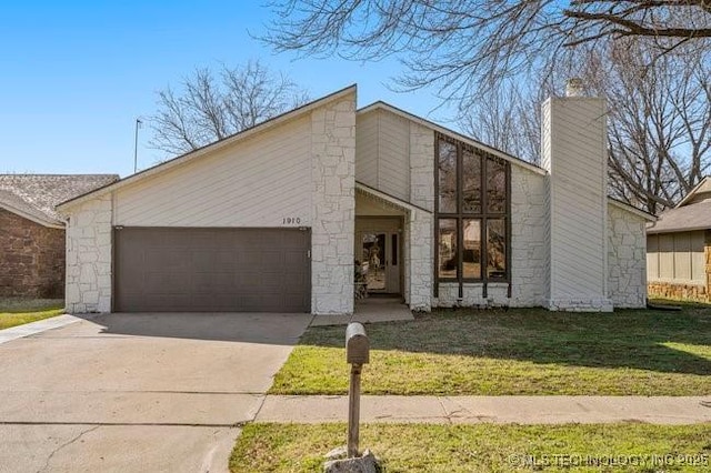 mid-century inspired home featuring concrete driveway, a front yard, a chimney, stone siding, and an attached garage