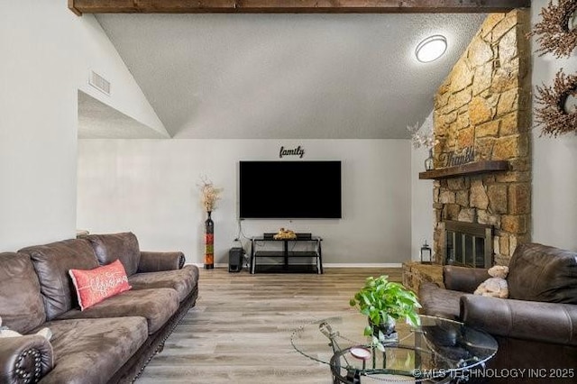 living area with visible vents, lofted ceiling with beams, a textured ceiling, light wood-style floors, and a stone fireplace