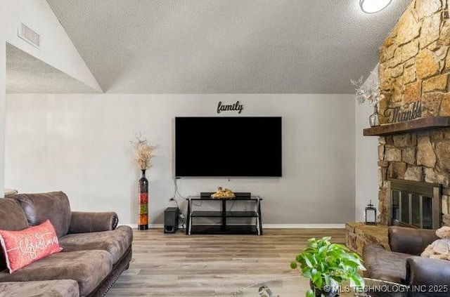 living room featuring visible vents, a textured ceiling, wood finished floors, a stone fireplace, and vaulted ceiling