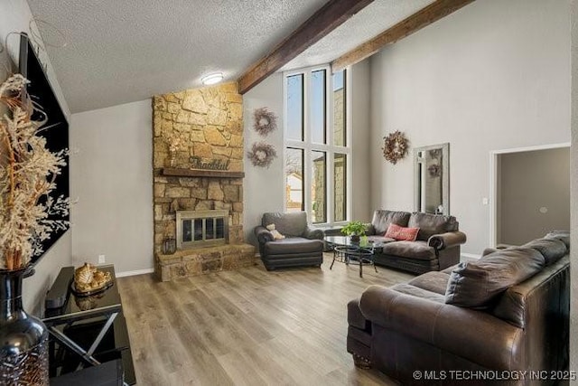 living room featuring high vaulted ceiling, beam ceiling, a stone fireplace, wood finished floors, and a textured ceiling