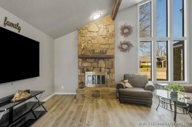 living room featuring a stone fireplace, wood finished floors, baseboards, and a textured ceiling