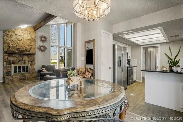 dining room with a stone fireplace, an inviting chandelier, light wood-style floors, and a textured ceiling