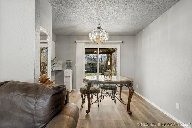 dining room featuring a notable chandelier, light wood-style flooring, a textured ceiling, and baseboards