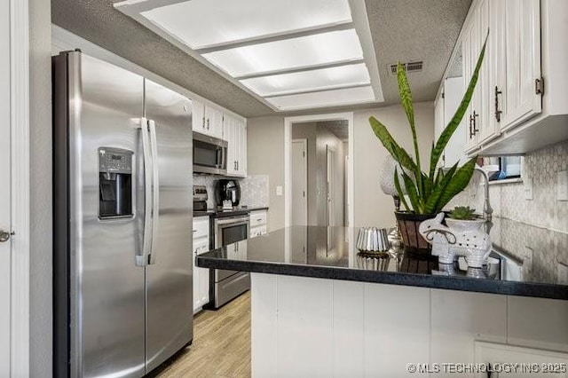 kitchen featuring a peninsula, decorative backsplash, appliances with stainless steel finishes, dark countertops, and light wood-type flooring