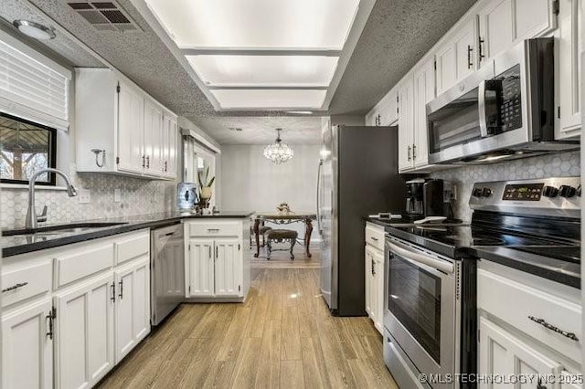 kitchen with a sink, stainless steel appliances, dark countertops, and white cabinets