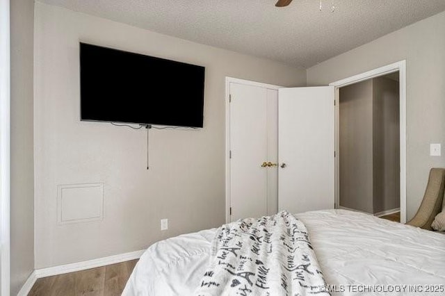 bedroom with a ceiling fan, a textured ceiling, wood finished floors, a closet, and baseboards