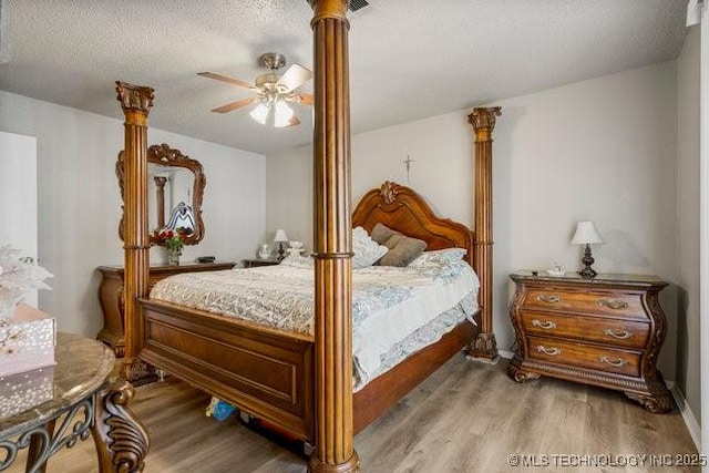 bedroom featuring a ceiling fan, wood finished floors, ornate columns, and a textured ceiling