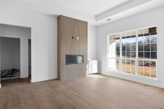 unfurnished living room with a tray ceiling, wood finished floors, and visible vents