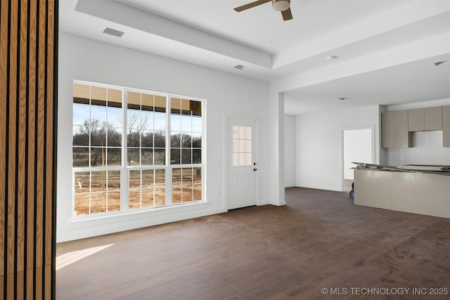 unfurnished living room with visible vents, a raised ceiling, dark wood-style floors, baseboards, and ceiling fan