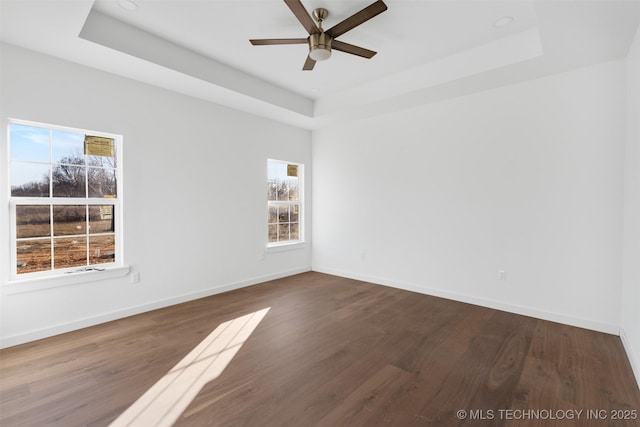 unfurnished room with baseboards, a tray ceiling, and dark wood-style flooring