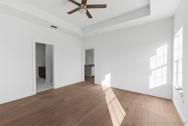 interior space featuring visible vents, a ceiling fan, a tray ceiling, wood finished floors, and baseboards