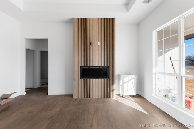 unfurnished living room featuring a tray ceiling, baseboards, a healthy amount of sunlight, and wood finished floors