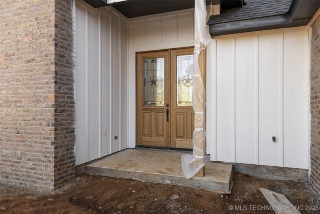 doorway to property with brick siding and a shingled roof