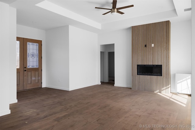 unfurnished living room with a raised ceiling, wood finished floors, and baseboards