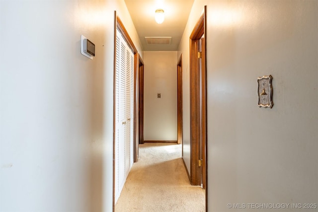 hall with attic access, light colored carpet, visible vents, and baseboards