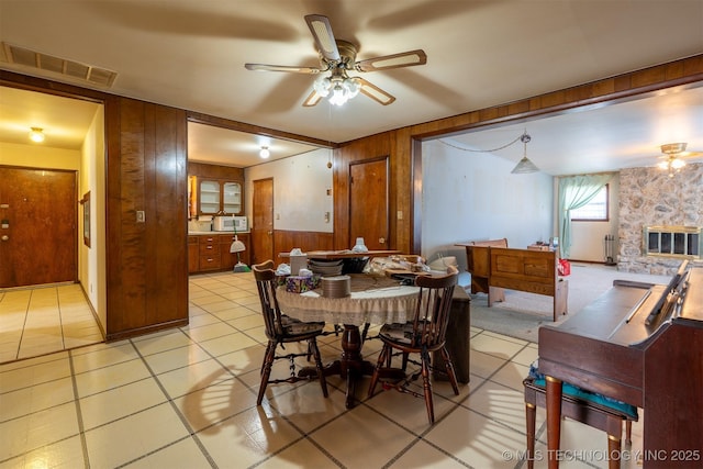 dining area with light tile patterned floors, visible vents, wooden walls, and a ceiling fan