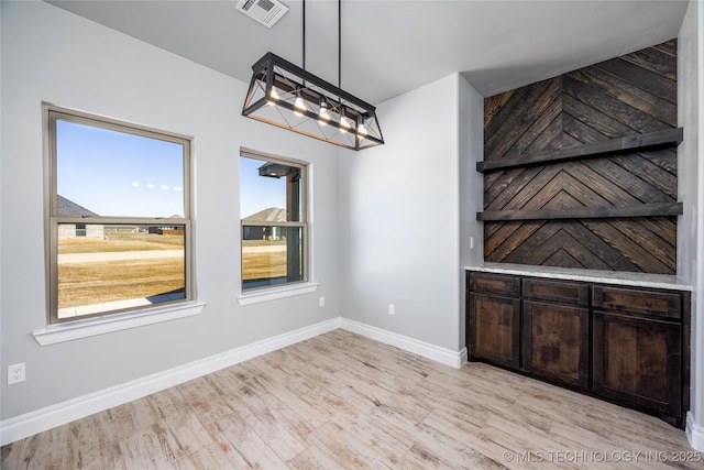 unfurnished dining area featuring visible vents, baseboards, a notable chandelier, and light wood finished floors