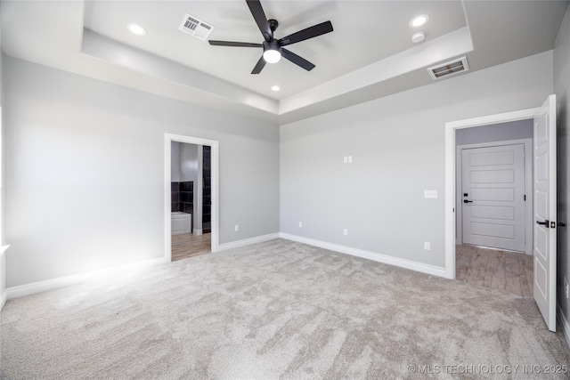 unfurnished bedroom featuring a tray ceiling, recessed lighting, visible vents, and carpet floors