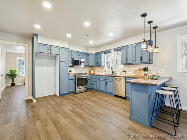 kitchen featuring blue cabinets, tasteful backsplash, appliances with stainless steel finishes, and a peninsula