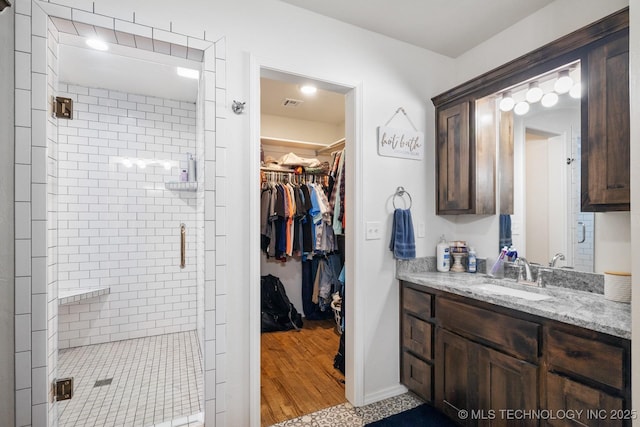 full bathroom with vanity, baseboards, visible vents, a shower stall, and a walk in closet