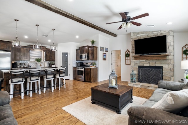 living room with a stone fireplace, lofted ceiling with beams, light wood-style floors, and visible vents