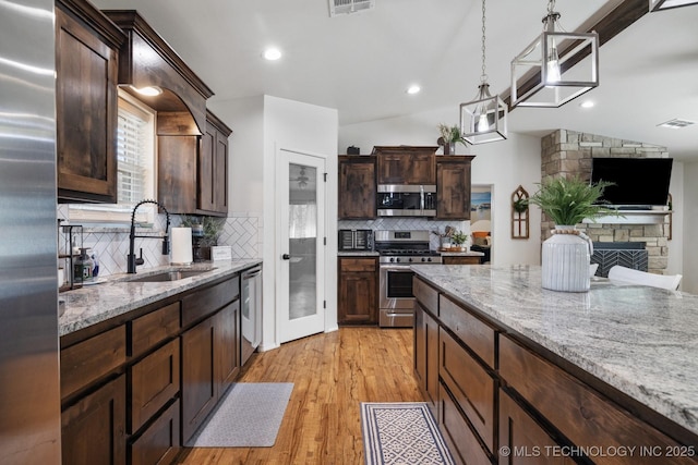 kitchen with light stone countertops, pendant lighting, light wood-type flooring, appliances with stainless steel finishes, and a sink