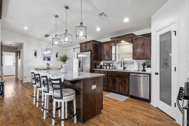 kitchen with visible vents, dark brown cabinets, a center island, appliances with stainless steel finishes, and a sink