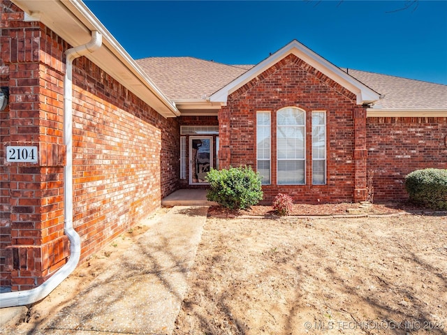 doorway to property featuring brick siding and roof with shingles