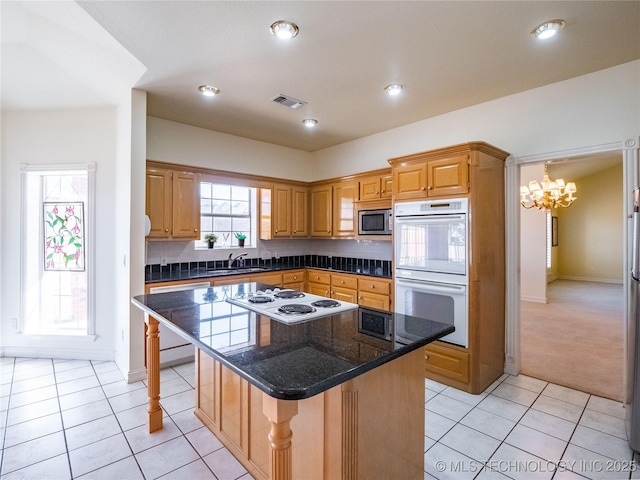 kitchen with a center island, a chandelier, light tile patterned floors, white appliances, and a sink