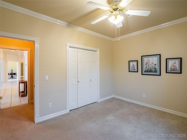 unfurnished bedroom featuring ceiling fan, baseboards, carpet, ornamental molding, and a closet