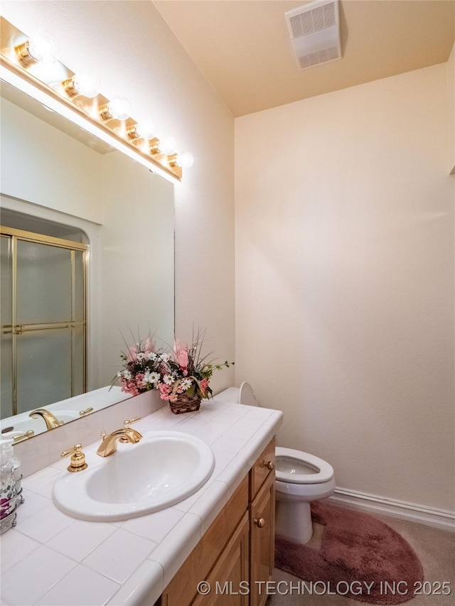 bathroom featuring vanity, a shower with shower door, baseboards, visible vents, and toilet