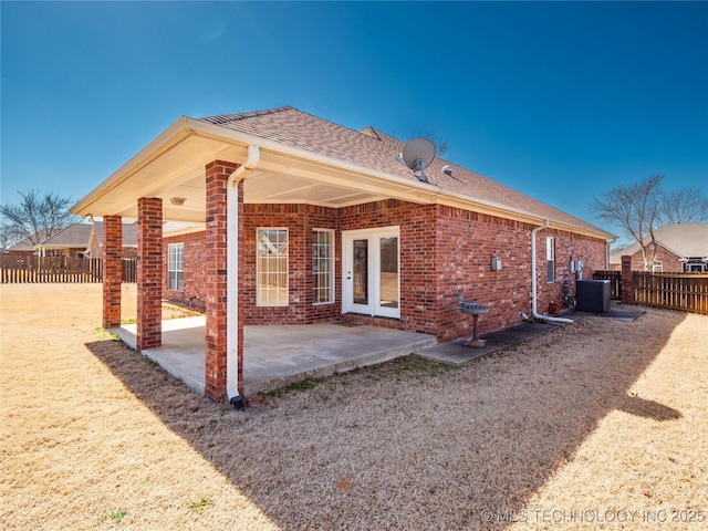 rear view of property with fence, roof with shingles, brick siding, central AC unit, and a patio area