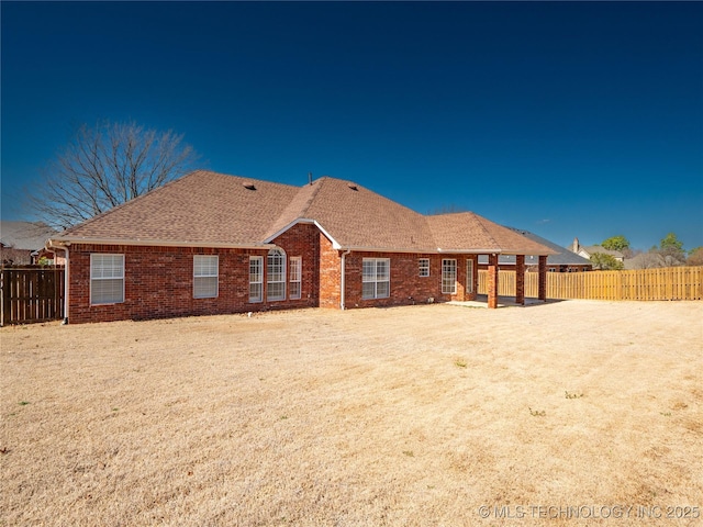 rear view of house featuring brick siding, fence private yard, and a shingled roof