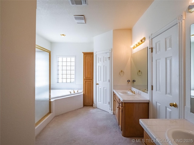 full bath featuring two vanities, a bath, visible vents, and a sink