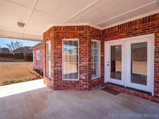 view of exterior entry with a patio, brick siding, and fence