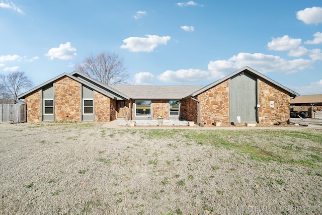 view of front facade featuring stone siding, a front lawn, and fence